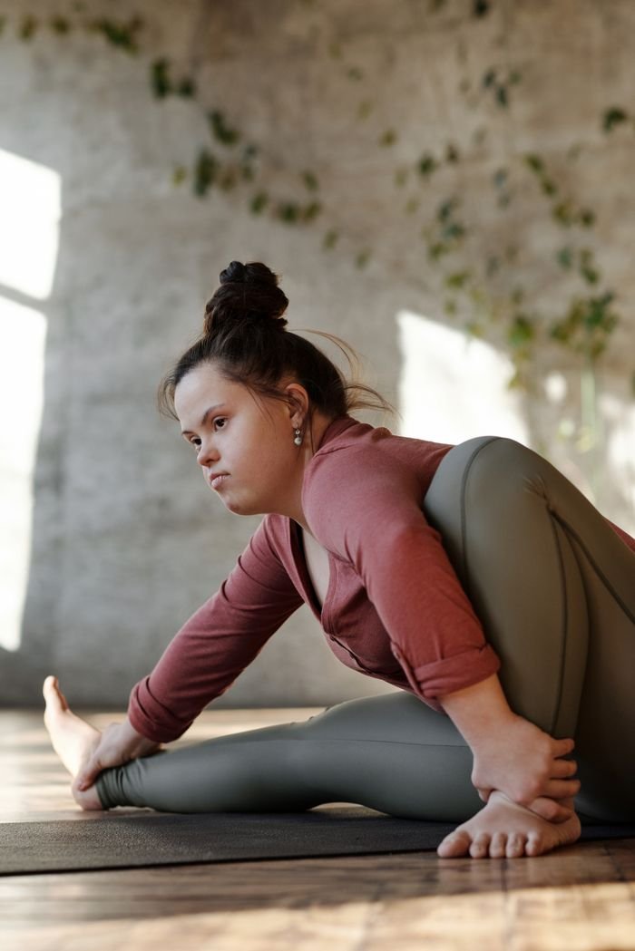 Woman with Down syndrome practicing yoga in a serene indoor setting, embodying focus and flexibility.